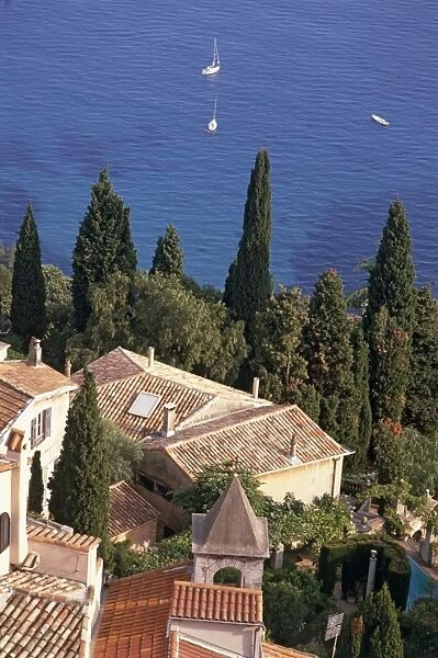 France, Provence, Roquebrune, rooftops of houses on steep hillside, tall trees and boat in sea seen from castle