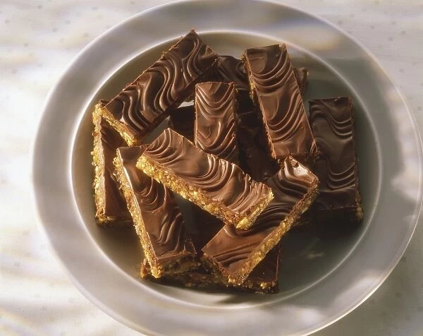 Fruit and nut bars covered with chocolate topping, served on plate, high angle view