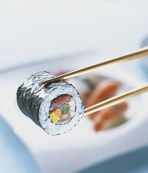 Futo maki zushi, cylindrical sushi parcel up held with chopsticks, close-up