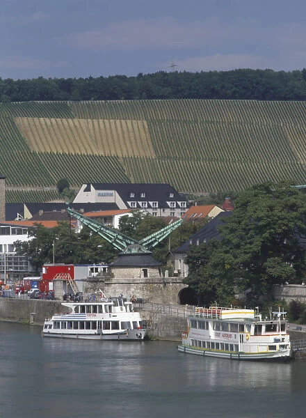 Germany, Bavaria, an old crane near Alte Mainbrucke over the river Main with vineyards on the hillside in the background