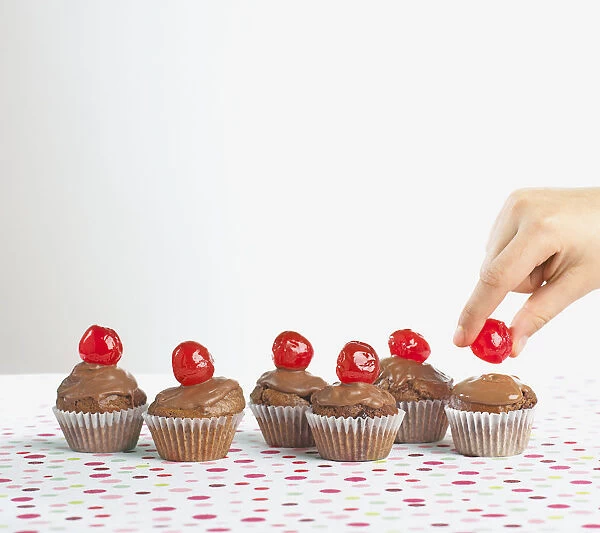 Girl placing red cherry on top of chocolate cupcake, close-up