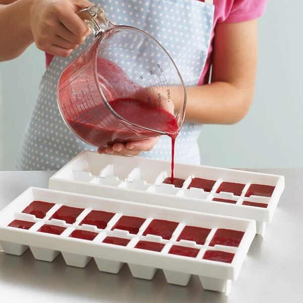 Girl pouring fresh raspberry juice into ice cube trays