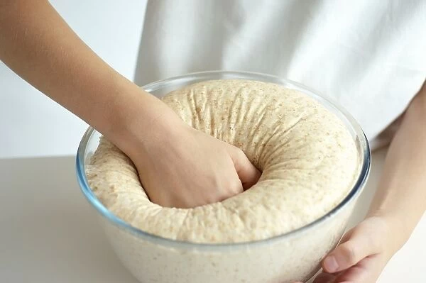 Girl punching risen dough in bowl, close-up