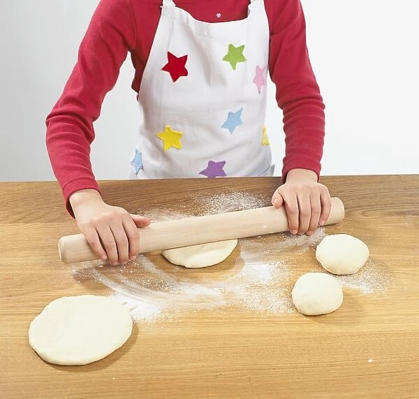 Girl rolling dough and flour with wooden rolling pin on kitchen worktop