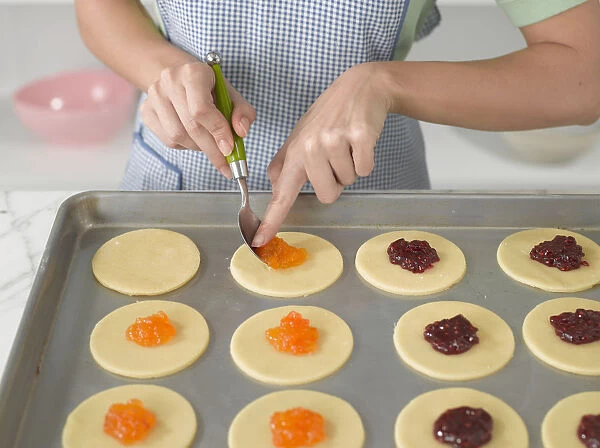 Girl spooning jam onto Hamantaschen dough, on baking tray, close-up