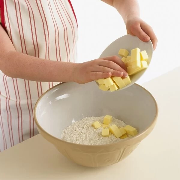 Girl using hands to add butter from white bowl on top of flour in mixing bowl