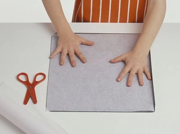 Girls hands placing baking paper on baking tray, pair of scissors nearby