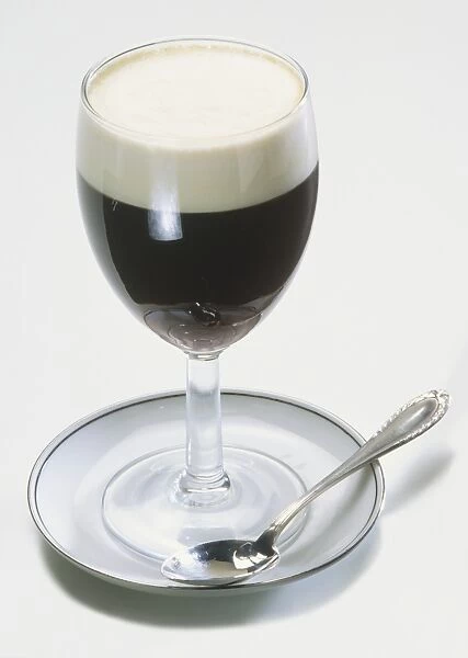 Glass of Irish coffee topped with cream, on saucer with teaspoon