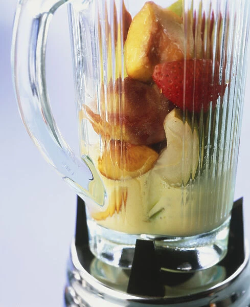 Glass jar of electric juicer filled with pieces if fresh fruit, close up