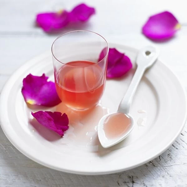 Glass of rose petal syrup, with spoon and petals on a plate