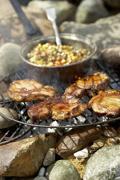 Glazed pork medallions on barbecue grill, and saucepan containing sweetcorn and pepper