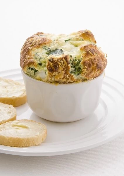 Golden puffy spinach souffle in bowl next to baguette slices