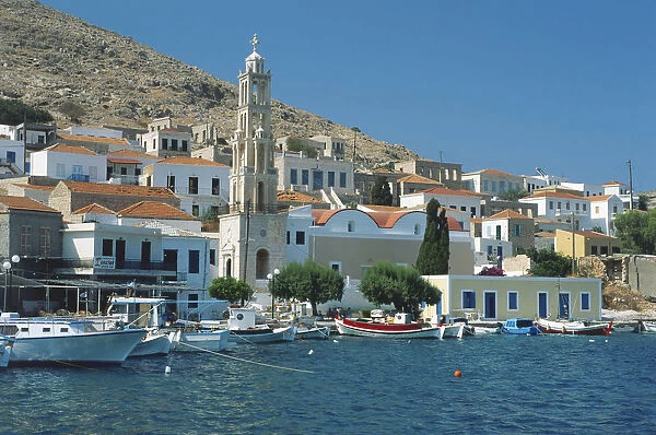 Greece, Chalki, Nimporio harbour with Agios Nikolaos church towering above the surrounding, colourful buildings, small boats moored along waterfront