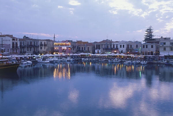 Greece, Crete, Rethymno, tavernas and bars along waterfront, at night, lights reflecting in the water, small boats moored