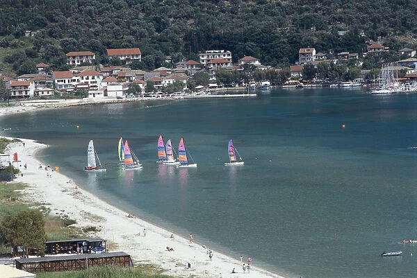 Greece, Ionian islands, Vasiliki, sailing boats with brightly coloured sails, white-sand beach, villas in background on hillside