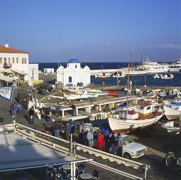 Greece, Mykonos, harbour in the early morning with local men preparing for work, blue domed church on port
