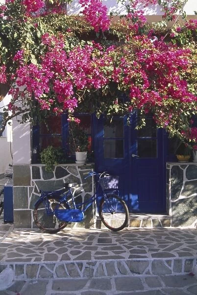 Greece, Paros, bougainvillea in Antiparos town, bicycle resting against mosaic-type wall