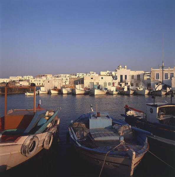 Greece, Paros, caiques at Naousa fishing harbour at sunset, small boats moored, buildings across water