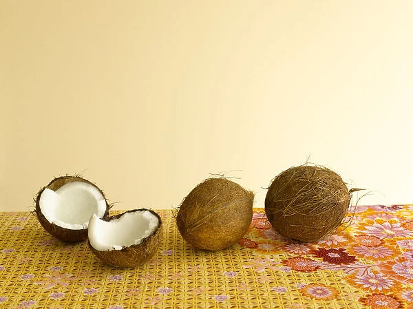 Whole and halved coconuts on floral tablecloth