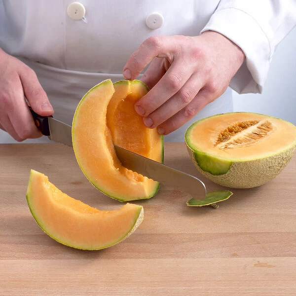 Hand cutting cantaloupe melon into slices with large kitchen knife, close-up