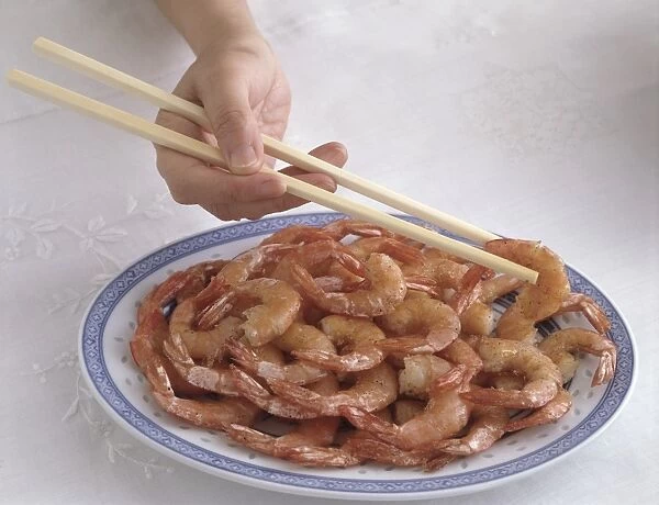 Hand holding chopsticks correctly over plate of sweet and sour prawns