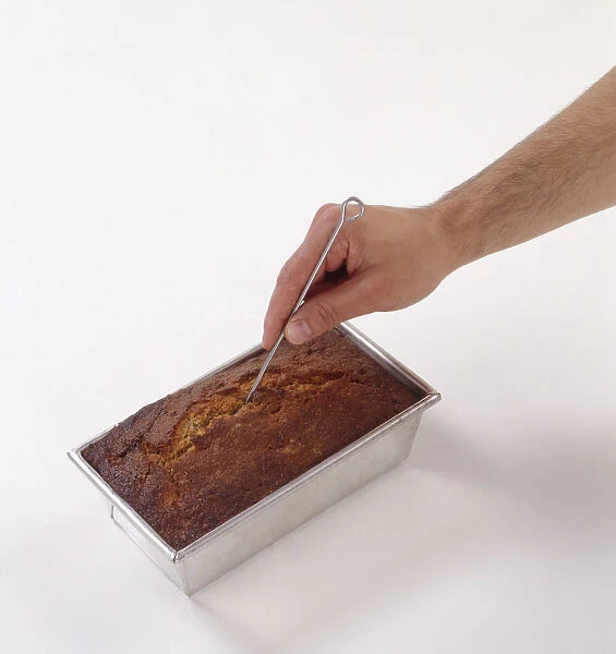Hand inserting metal skewer in baked cake in cake tin, close-up