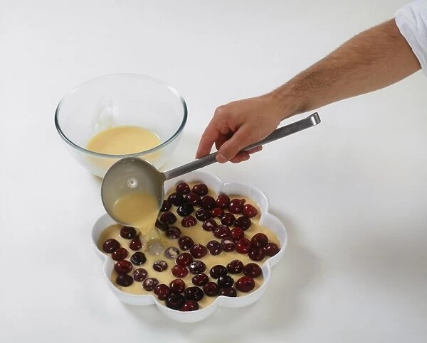 Hand pouring batter over cherries for making cherry clafoutis