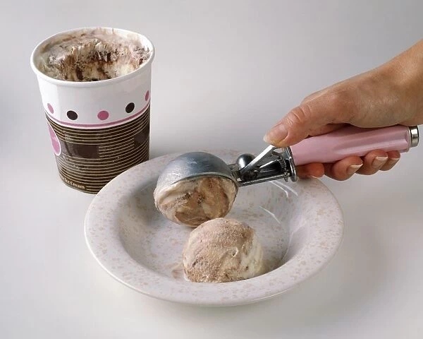 Hand scooping ice cream into bowl, tub of ice cream nearby