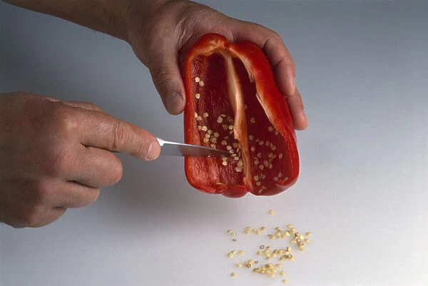 Hand scraping out seeds from halved red bell pepper, using paring knife, close-up