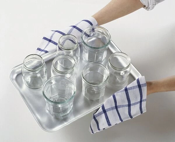 Hands holding hot empty glass jars on stainless steel baking tray using tea towel