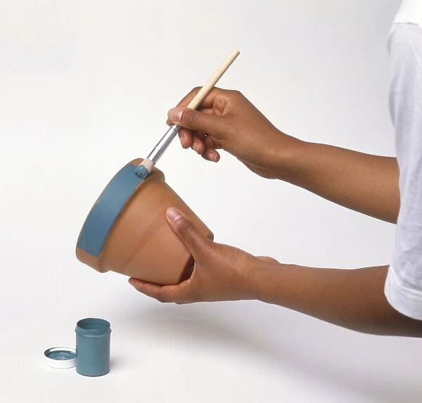 Hands painting a plant pot with blue paint