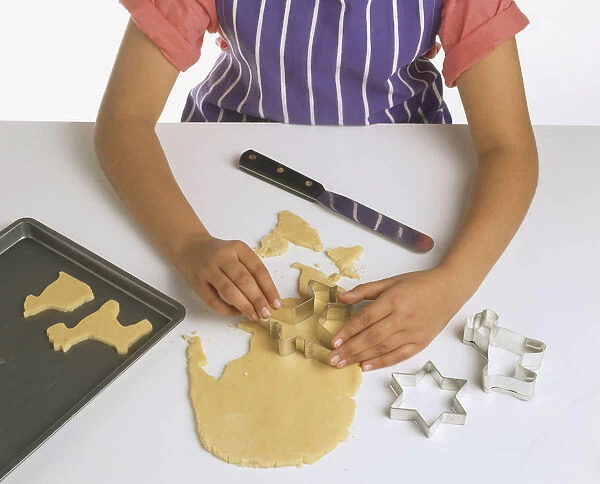 Hands of person cutting rolled cookie dough into shapes, high angle view