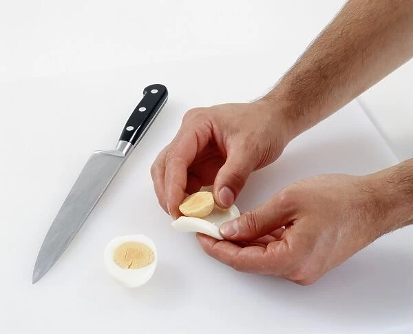 Hands separating boiled egg, chefs knife nearby, close-up