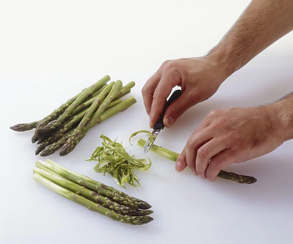 Hands shaving asparagus with a peeler, piles of asparagus stems