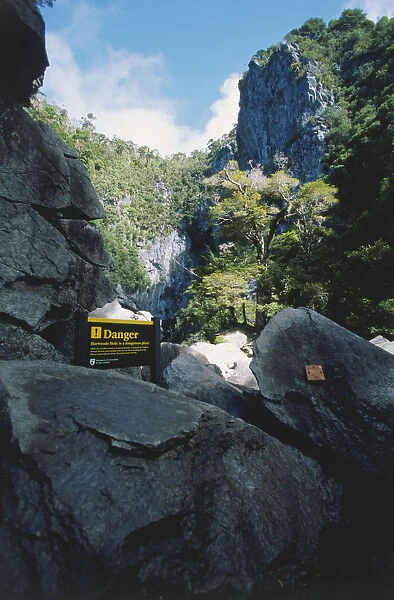 Harwoods Hole, a vertical marble shaft, with a danger or warning sign in the foreground, in the Abel Tasman National Park, South Island, New Zealand
