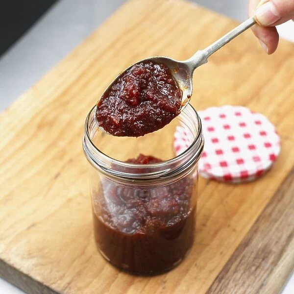 Holding spoon of homemade tomato chutney above glass jar