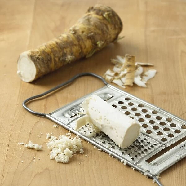 Horseradish root, peel, and partially grated on metal grater, on wooden surface