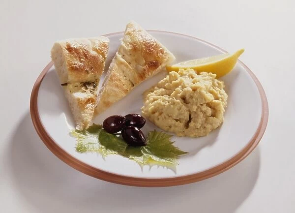 Hummus served on plate with focaccia bread, black olives, slice of lemon and vine leaf