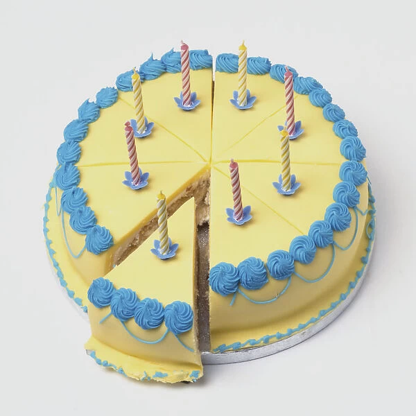 Iced birthday cake decorated with eight candles, one slice partially pulled out from centre, high angle view