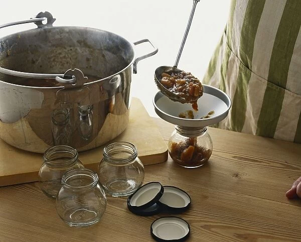 Ladling hot chutney into jar through funnel on wooden worktop