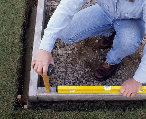 Laying a patio, using a spirit level and hammer to tap concrete edging level, close-up