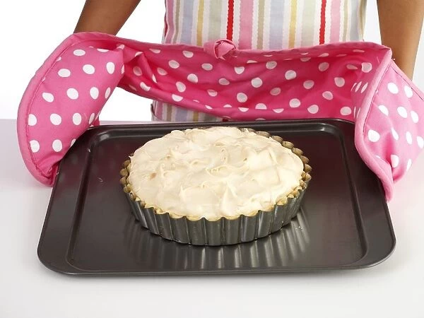 Lemon meringue pie on baking tray, girl holding baking tray, wearing oven gloves, close-up