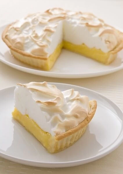 Lemon meringue pie on plate, single slice on plate in foreground, close-up