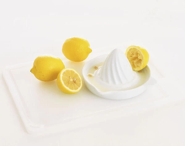 Two whole lemons and a halved lemon, with squeezed half resting on white china lemon juicer