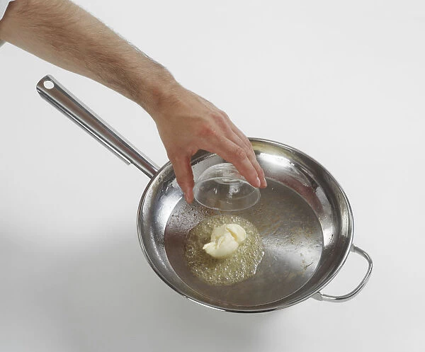 Man holding small glass bowl above butter melting in frying pan
