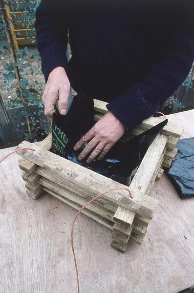 Man making a wooden hanging basket lining it with strips of polythene