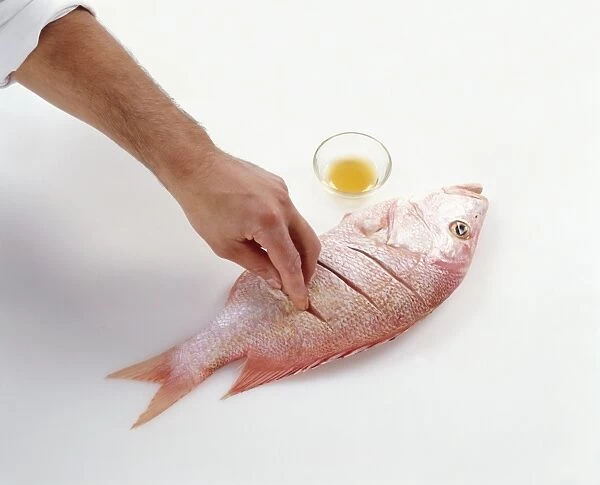 Man rubbing Chinese Rice wine into diagonal cuts in raw red snapper