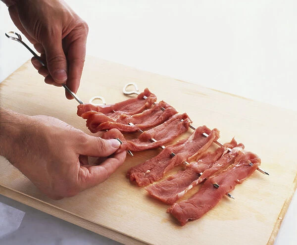 Man skewering pork fillets on wooden chopping board