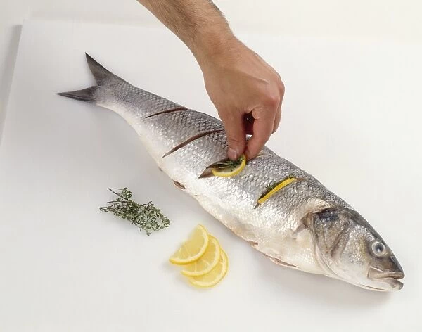Man stuffing whole fish with lemon slices and thyme
