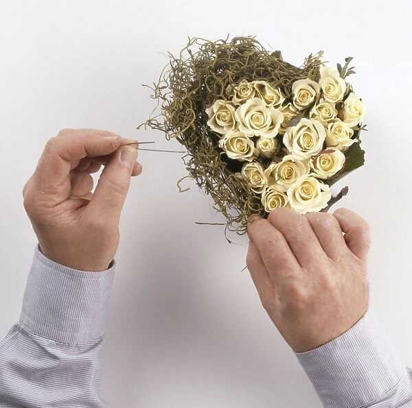 Mans hands creating heart-shaped flower arrangement with cream roses and dried moss